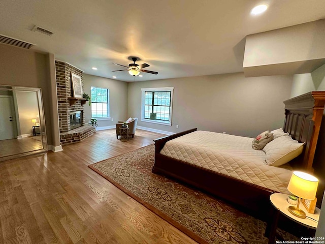 bedroom featuring brick wall, a brick fireplace, ceiling fan, and hardwood / wood-style floors