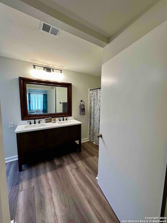 bathroom with hardwood / wood-style flooring, a textured ceiling, and dual bowl vanity