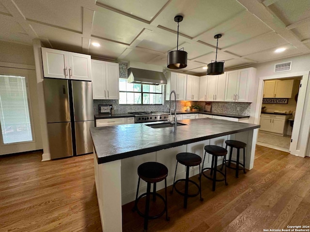 kitchen featuring wall chimney range hood, white cabinets, dark hardwood / wood-style flooring, a kitchen island with sink, and stainless steel appliances