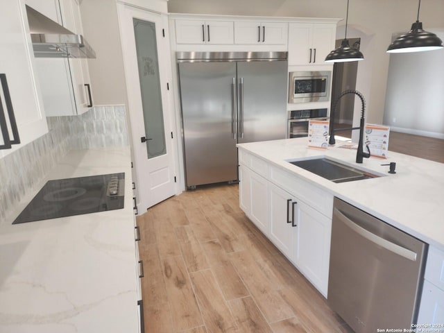 kitchen featuring built in appliances, sink, white cabinetry, and pendant lighting