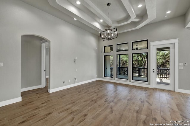 empty room with an inviting chandelier, wood-type flooring, a raised ceiling, and a high ceiling