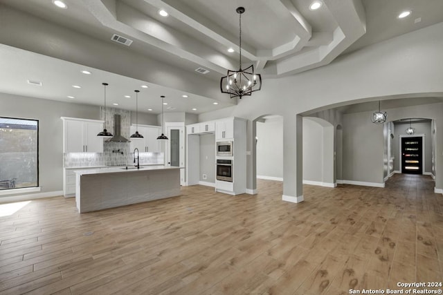 unfurnished living room with a raised ceiling, a high ceiling, sink, and light hardwood / wood-style floors