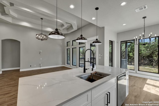 kitchen featuring sink, dishwasher, hanging light fixtures, light stone counters, and white cabinets