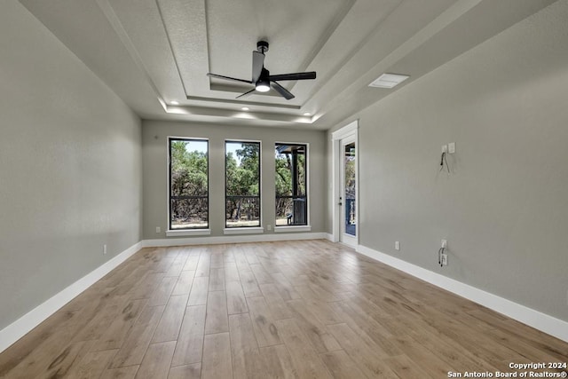 empty room with a raised ceiling, ceiling fan, and light wood-type flooring