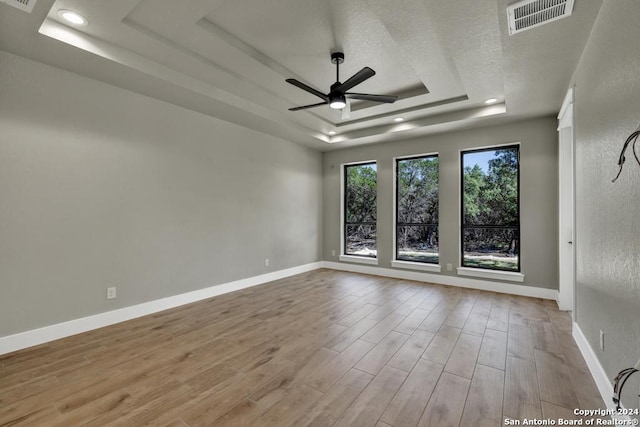 unfurnished room featuring a raised ceiling, ceiling fan, a textured ceiling, and light hardwood / wood-style floors