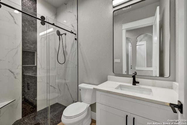 bathroom featuring a shower with door, vanity, and toilet