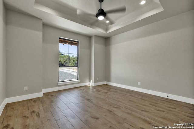 unfurnished room featuring light hardwood / wood-style flooring, ceiling fan, and a tray ceiling