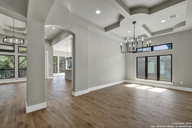 unfurnished dining area featuring a towering ceiling, hardwood / wood-style floors, coffered ceiling, a notable chandelier, and beam ceiling