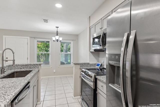 kitchen with decorative light fixtures, stainless steel appliances, sink, light stone counters, and light tile patterned floors