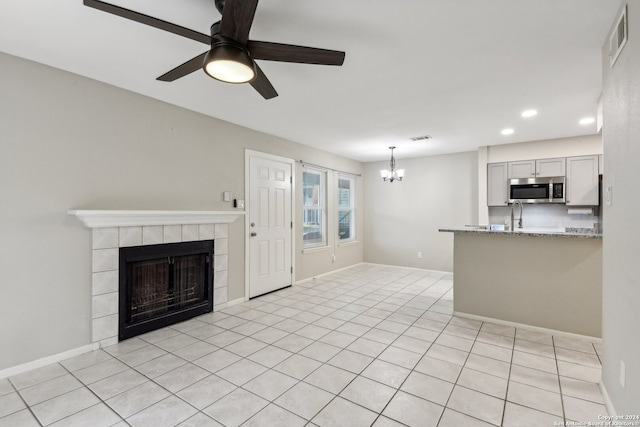 unfurnished living room with ceiling fan with notable chandelier, a tiled fireplace, and light tile patterned floors