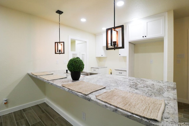 kitchen featuring light stone countertops, pendant lighting, white cabinets, and kitchen peninsula