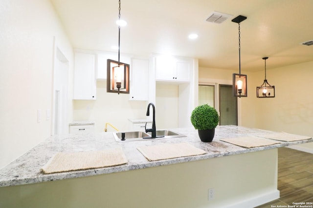 kitchen with dark hardwood / wood-style floors, a kitchen island, pendant lighting, white cabinetry, and light stone countertops