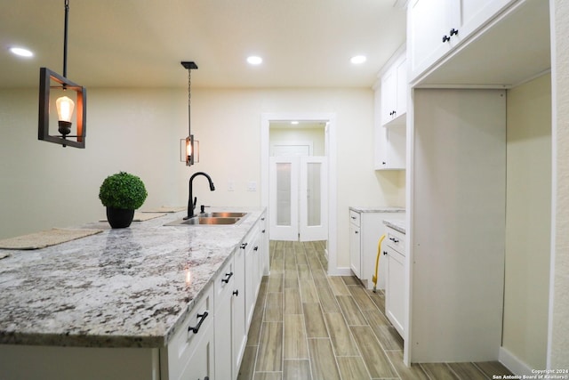 kitchen with pendant lighting, white cabinets, light stone counters, and sink