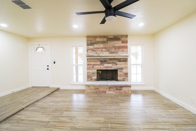 unfurnished living room featuring ceiling fan and a stone fireplace