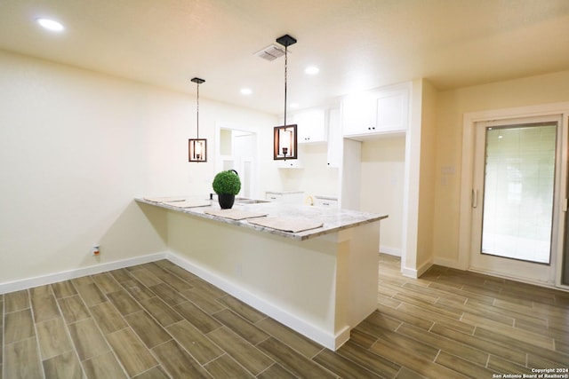 kitchen with a kitchen bar, kitchen peninsula, pendant lighting, white cabinets, and light stone counters