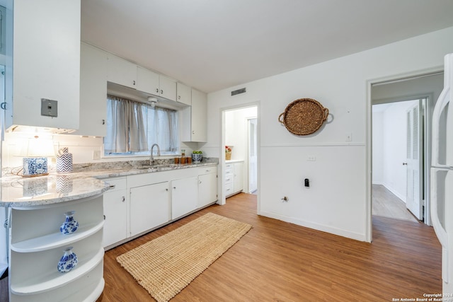 kitchen with light stone counters, light hardwood / wood-style floors, sink, and white cabinets