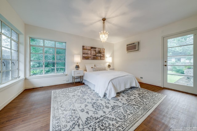 bedroom with multiple windows, wood-type flooring, a wall mounted AC, and an inviting chandelier