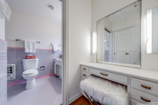 bathroom with vanity, heating unit, tile walls, and toilet