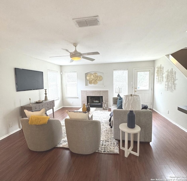 living room featuring ceiling fan, plenty of natural light, a tile fireplace, and dark hardwood / wood-style floors