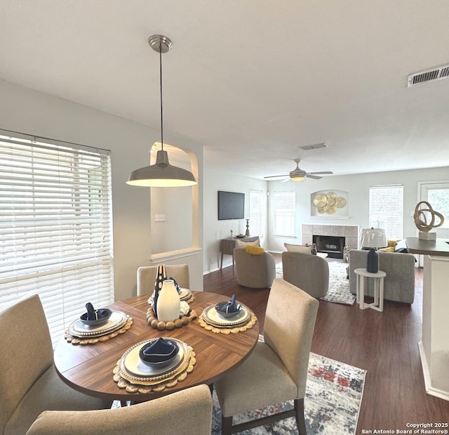 dining area with ceiling fan, a healthy amount of sunlight, and a tiled fireplace