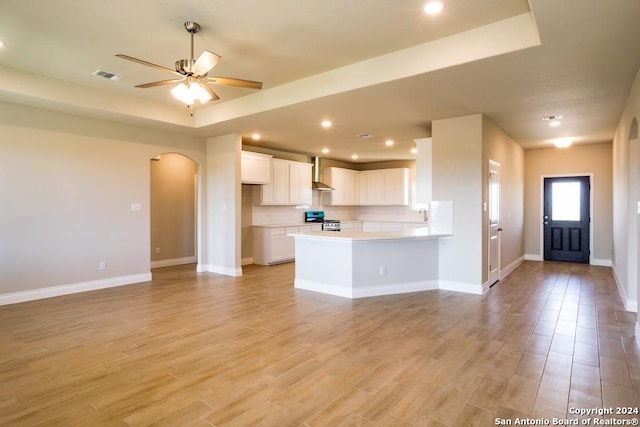 kitchen with white cabinetry, stainless steel range oven, ceiling fan, kitchen peninsula, and wall chimney range hood