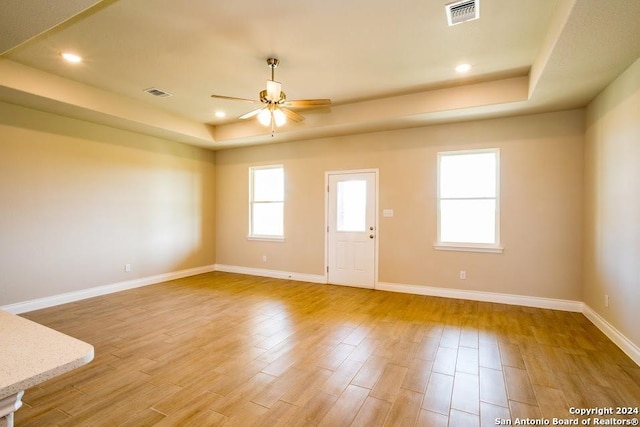 unfurnished room featuring light hardwood / wood-style floors, ceiling fan, and a raised ceiling