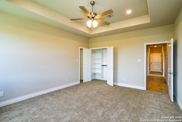 unfurnished bedroom featuring ceiling fan, a tray ceiling, a closet, and carpet