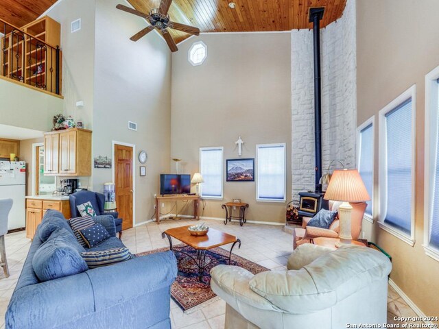 tiled living room with ceiling fan, a wood stove, high vaulted ceiling, and wooden ceiling