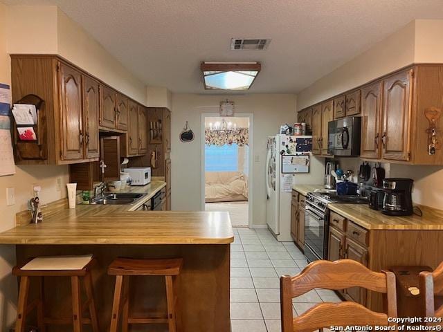 kitchen with range, a kitchen breakfast bar, light tile patterned flooring, kitchen peninsula, and white fridge