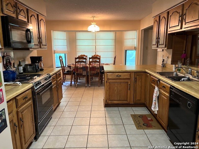 kitchen with black appliances, sink, light tile patterned floors, kitchen peninsula, and a textured ceiling