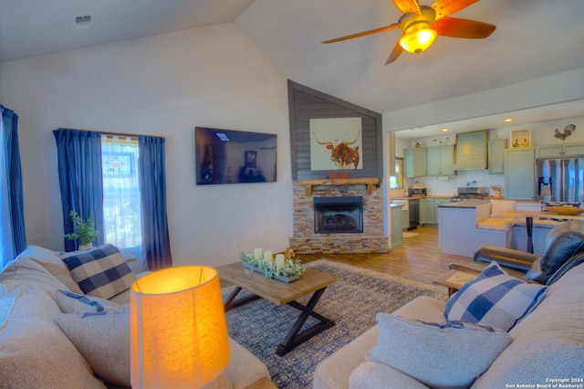 living room with light hardwood / wood-style flooring, a stone fireplace, high vaulted ceiling, and ceiling fan