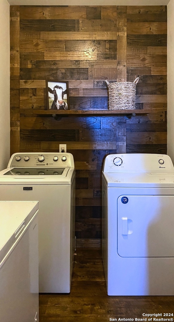 washroom featuring wooden walls, washer and dryer, and dark wood-type flooring