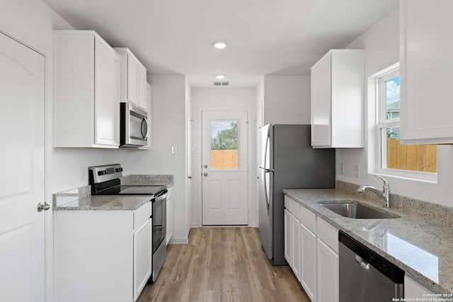 kitchen with appliances with stainless steel finishes, white cabinetry, sink, light hardwood / wood-style floors, and light stone countertops