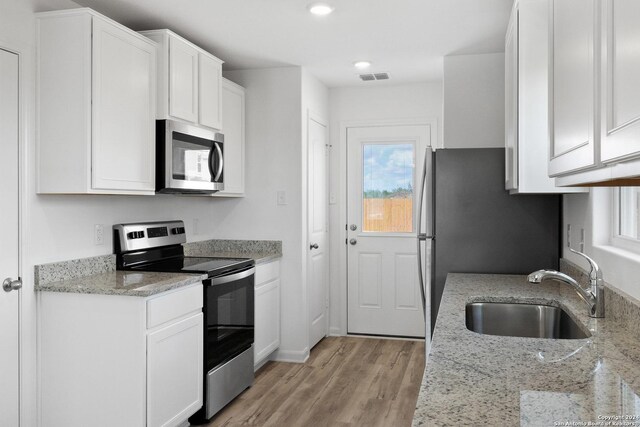 kitchen with stainless steel appliances, white cabinetry, sink, and light stone countertops