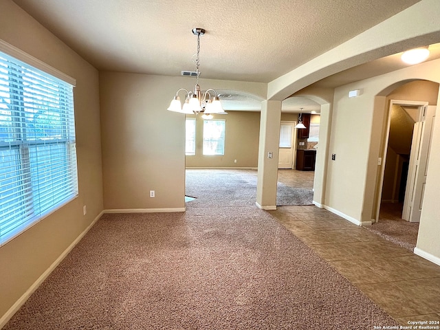 tiled empty room with a textured ceiling and a chandelier