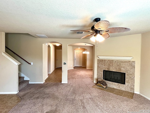 unfurnished living room featuring a textured ceiling, carpet, a tiled fireplace, and ceiling fan