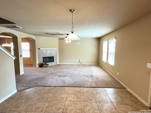 unfurnished living room with a textured ceiling, a tiled fireplace, light tile patterned floors, and ceiling fan with notable chandelier