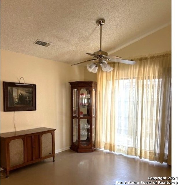 unfurnished dining area featuring vaulted ceiling, a textured ceiling, ceiling fan, and a wealth of natural light