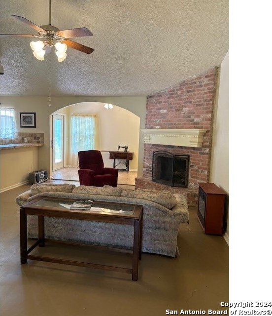 living room with a fireplace, concrete flooring, a textured ceiling, and ceiling fan