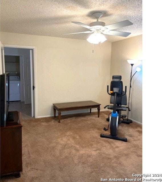 exercise area with a textured ceiling, washer / dryer, light colored carpet, and ceiling fan