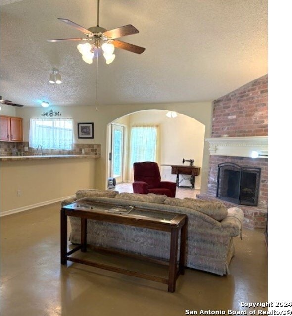 living room featuring a textured ceiling, brick wall, a fireplace, and ceiling fan