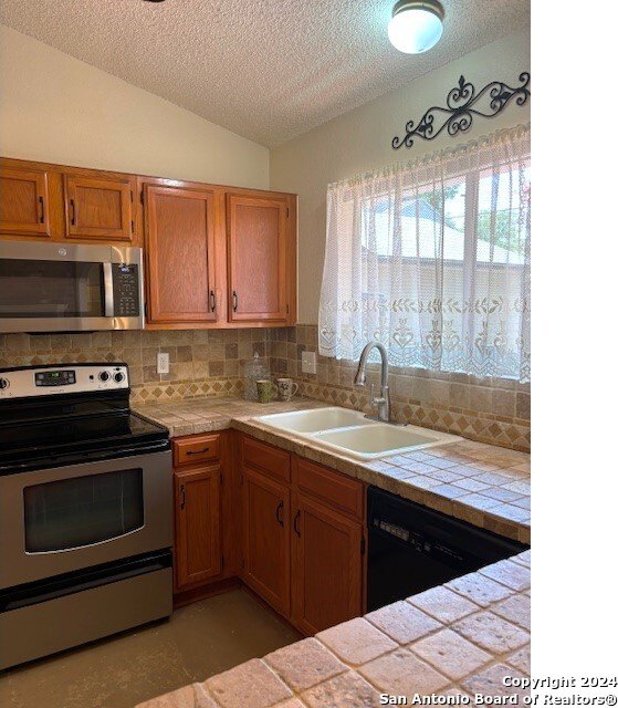 kitchen with sink, decorative backsplash, tile counters, and stainless steel appliances