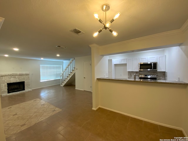 kitchen featuring appliances with stainless steel finishes, tasteful backsplash, white cabinets, a stone fireplace, and crown molding