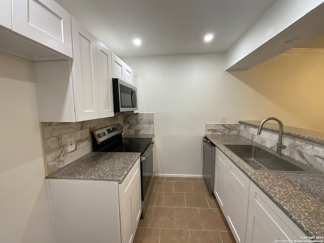 kitchen with tasteful backsplash, dark tile patterned floors, white cabinets, sink, and appliances with stainless steel finishes