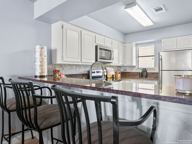 kitchen featuring a breakfast bar, appliances with stainless steel finishes, kitchen peninsula, and white cabinets