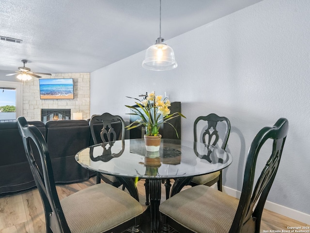 dining area with light hardwood / wood-style flooring, ceiling fan, a fireplace, and a textured ceiling