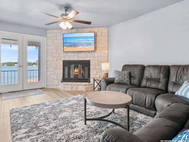 living room with hardwood / wood-style flooring, a water view, a stone fireplace, and ceiling fan