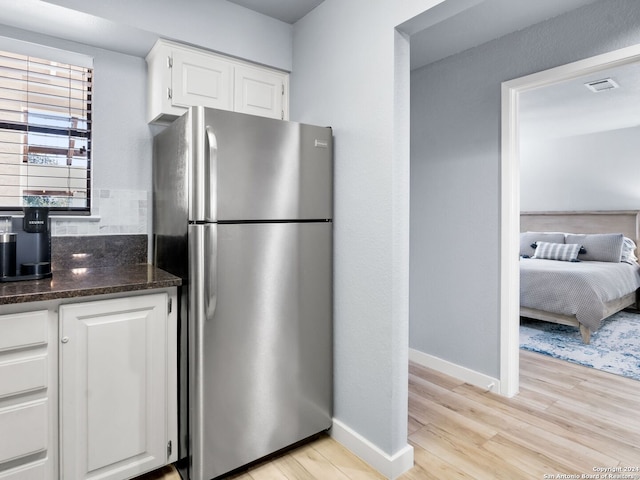 kitchen featuring stainless steel refrigerator, dark stone counters, light hardwood / wood-style flooring, and white cabinets