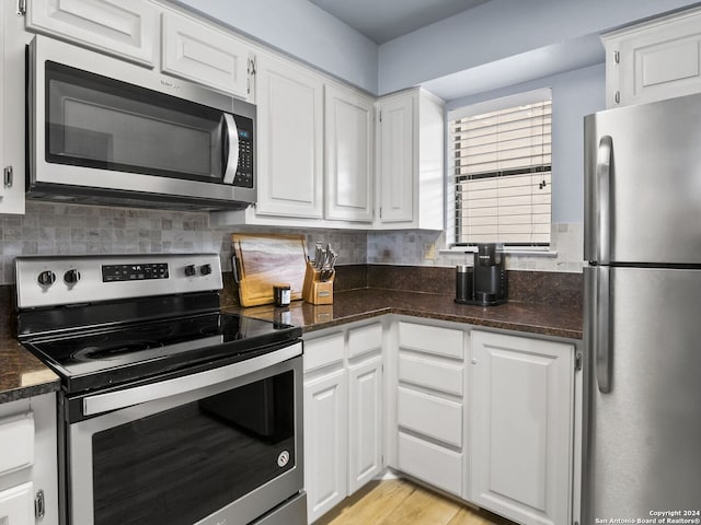 kitchen with tasteful backsplash, dark stone counters, stainless steel appliances, light hardwood / wood-style floors, and white cabinets