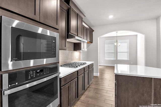 kitchen with a chandelier, appliances with stainless steel finishes, pendant lighting, decorative backsplash, and dark brown cabinetry